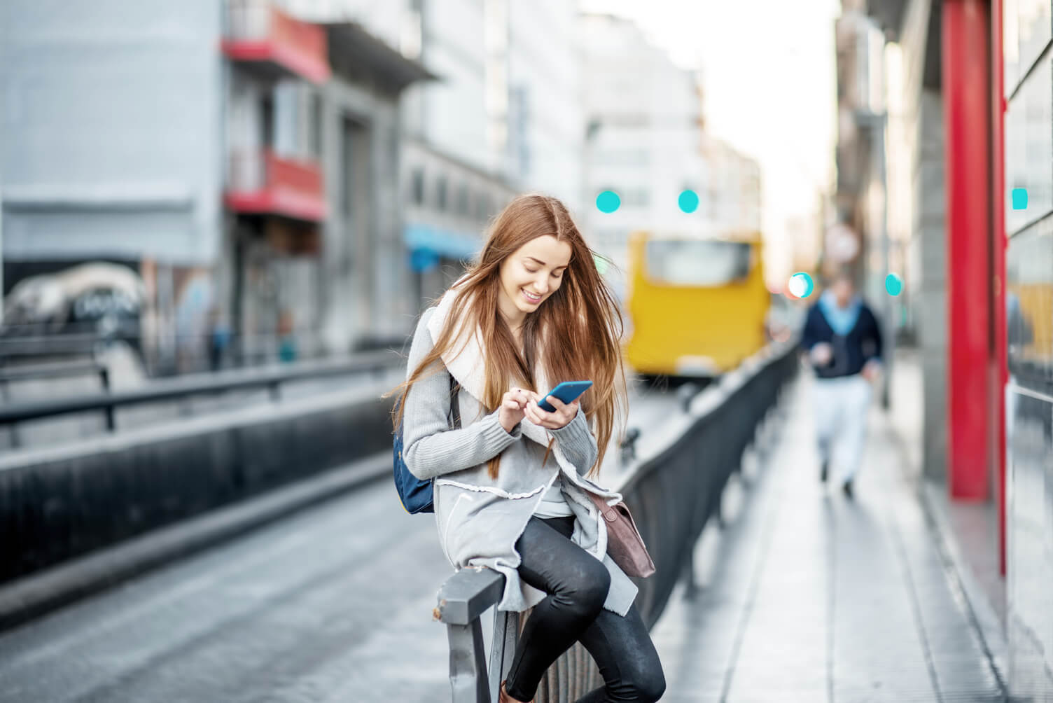 Woman is wearing a thin, gray sweater with a white shirt and red, orange high wasted skirt. She is leaning on a pole outside in an urban environment. She  has short brown hair which is pulled back into a small, lower ponytail. She apperas to be of Asain desecent. 