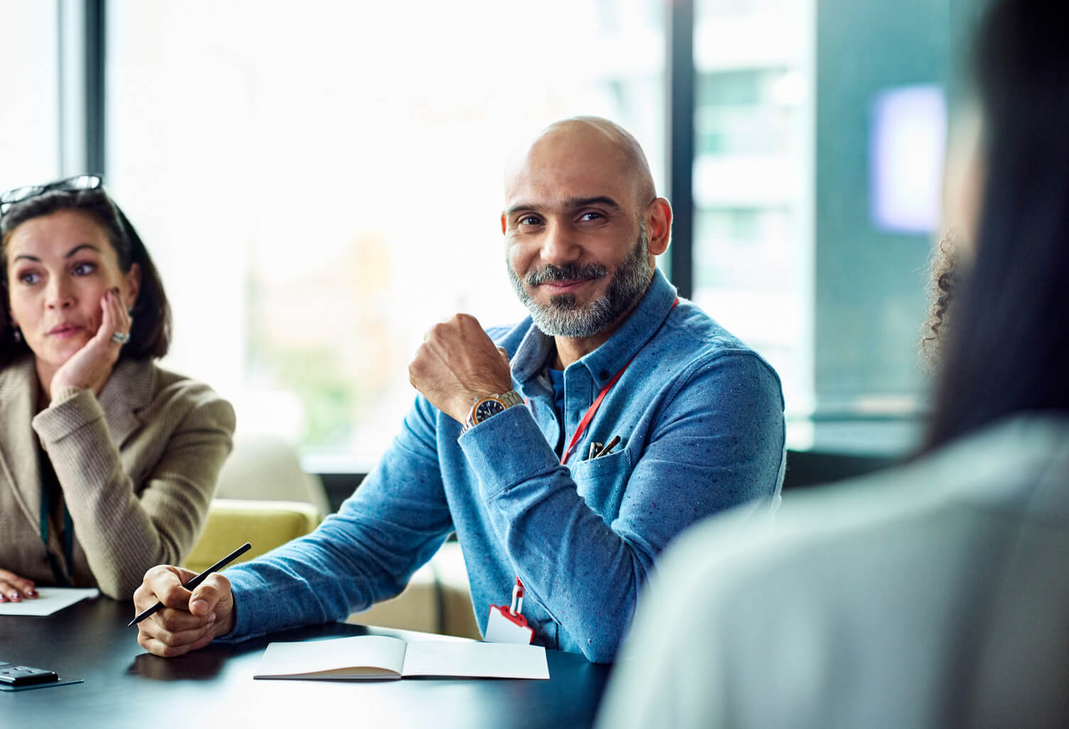 People seated at a conference table in a bright office, taking notes and discussing during a meeting.